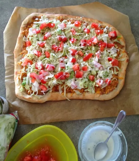 pizza topped with beans, cheese, lettuce, tomatoes and ranch